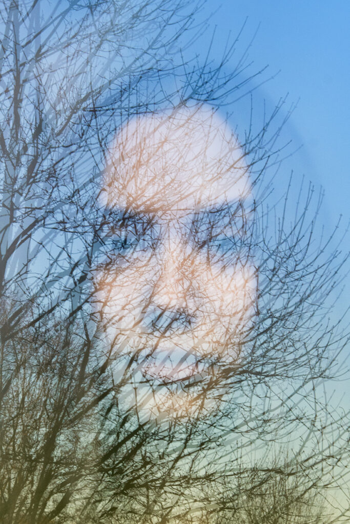 Foto portret van vrouw achter glas met reflectie van bomen en lucht.