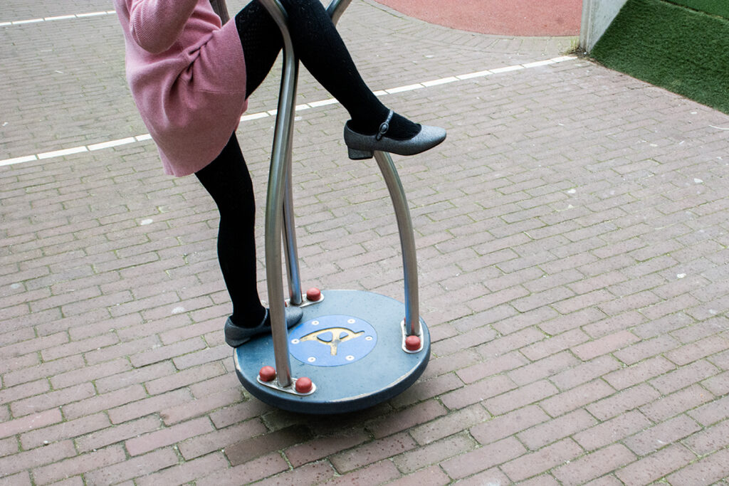 Straatfotografie van meisje met zwarte maillot op speelapparaat op pleintje. Straatfotografie.